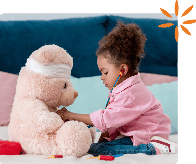Child using a toy stethoscope to examine a teddy bear wearing a bandage around its head.